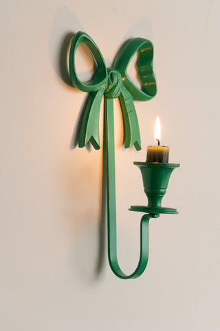 The Green Bow Wall-Mounted Candle Holder on the wall with a lit candle inside.