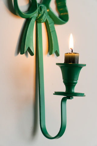 Close-up of the candle holder of the Green Bow Wall-Mounted Candle Holder, styled with a lit candle inside.