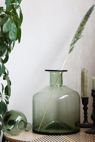 The Green Glass Apothecary Bottle styled with a dried stem inside, alongside some greenery and candlestick holders.