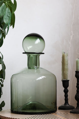 The Green Glass Apothecary Bottle styled alongside some candlestick holders and greenery.