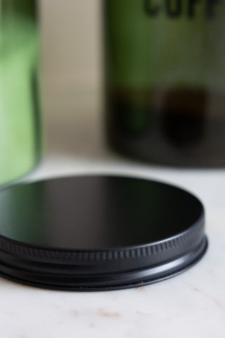 Close-up of the lid of the Green Glass Storage Jar With Black Lid - Coffee on a white marble surface.