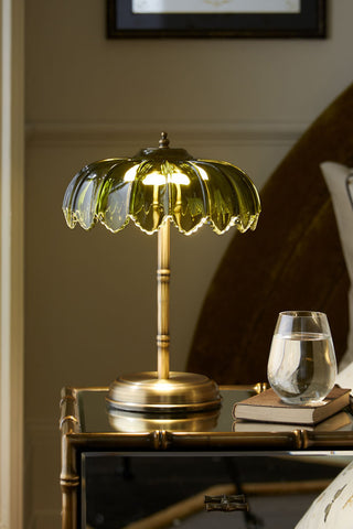 A palm table light displayed lit on a side table with a book and a glass of water.