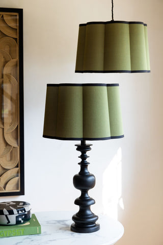 Two Green Scalloped Easyfit Lampshades, one displayed on a lamp base and one suspended as a pendant light, in front of a white wall, styled with some home accessories.