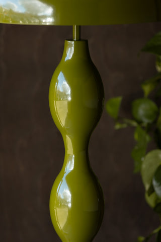 Close-up of the wavy detail on the Green Wavy Retro Floor Light, in front of a dark wall with some greenery.