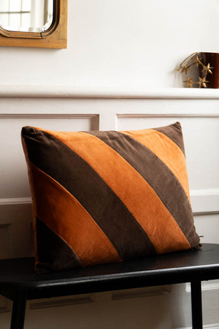 The HKLiving Coffee & Mocha Striped Velvet Cushion styled on a black seat in front of a panelled wall.