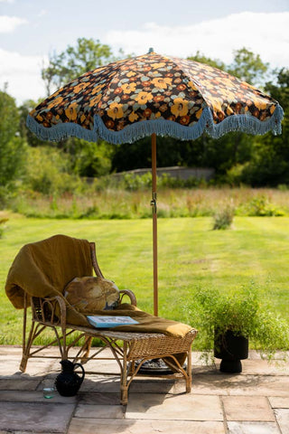 The HKliving Floral Flourish Parasol with Blue Fringing styled in the sunshine, next to a wicker sun lounger.