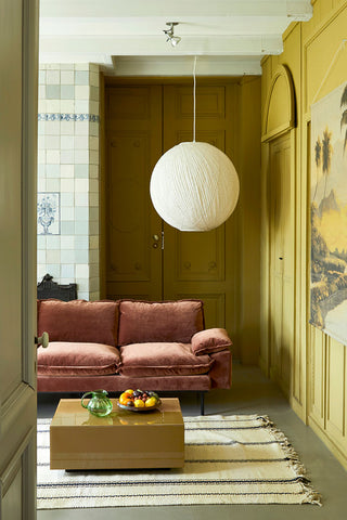 The HKliving Retro Sofa in Magnolia Velvet styled in a living room with a coffee table, rug and large pendant light, styled with various home accessories.