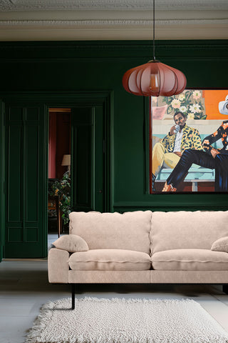 The HKliving Retro Sofa in Taupe Boucle styled on a rug in a living room with green walls, with an art print and a pendant light. 