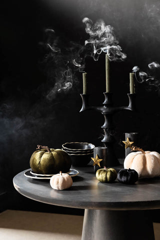 A round table decorated with Halloween pumpkins, tableware and candles, with smoke rising from the newly extinguished dinner candles.