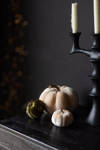 Three velvet pumpkin decorations arranged together on a wooden unit next to a candelabra.