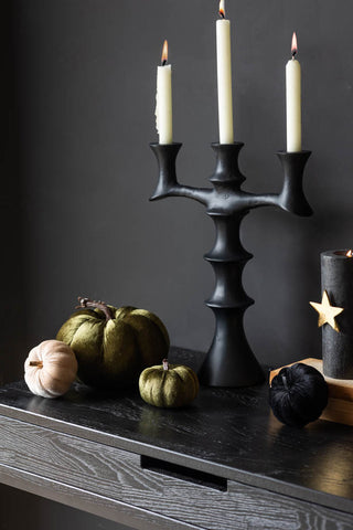 Four velvet pumpkins of different sizes and colours arranges together on a black table with a candelabra and candles.