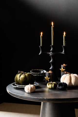 A round Halloween table styled with velvet pumpkins, tableware, candles and a candelabra.