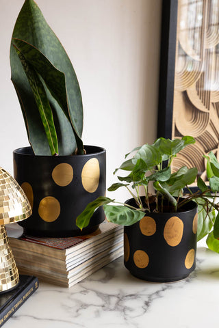 The Handcrafted Black & Metallic Planter in both sizes, styled with plants inside on a marble table, with books, an art print and a mushroom ornament.