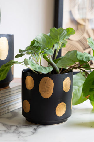 The Handcrafted Black & Metallic Planter In Small, styled on a white marble table with a plant inside, next to a stack of magazines.