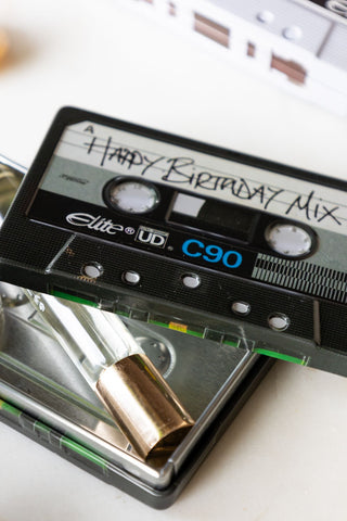 Close-up of the Happy Birthday Cassette Tape Storage Tin with the lid off, styled with some perfume inside.