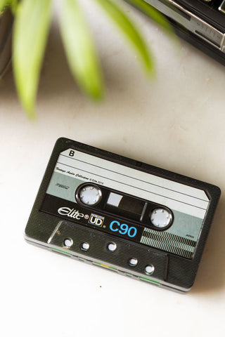 Close-up of the Happy Birthday Cassette Tape Storage Tin seen from above, styled with another tin and a plant.