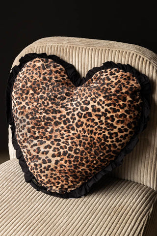 The Heart Leopard Print Velvet Ruffle Cushion styled on a chair.