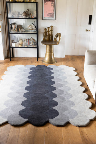 The Hexagonal Ombre Rug styled on a wooden floor in front of an armchair, chair and a shelving unit.