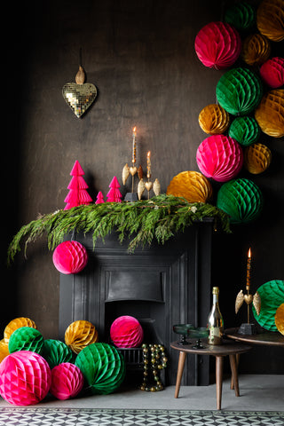 An amazing lifestyle of pink, gold and green honeycomb balls in a formation down a fireplace.