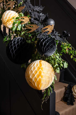 The Set Of 2 Black Honeycomb Ball Decorations styled with cream paper decorations hung on a black banister.