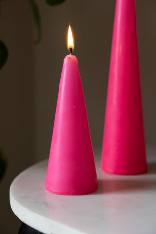 Close-up shot of the lit Small Hot Pink Cone Shaped Candle on a table, with the Large version in the background.