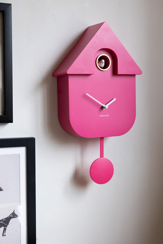 The Hot Pink Modern Cuckoo Wall Clock styled on the wall next to some framed artworks.