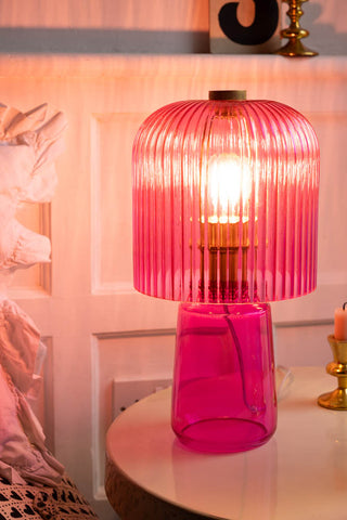 The Hot Pink Seventies Glass Table Lamp switched on and styled on a bedside table.