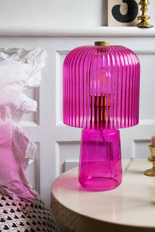 The Hot Pink Seventies Glass Table Lamp styled on a bedside table with various accessories.