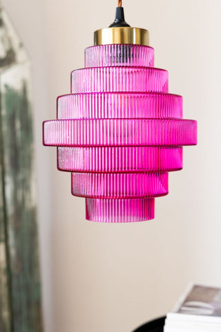 The Hot Pink Tiered Glass Easyfit Ceiling Shade hanging in front of a neutral wall.