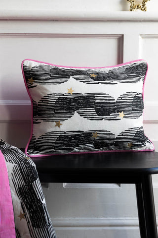 Image of the Hot Pink & Gold Star Print Reversible Cushion styled on a black bench against a white panelled backdrop.