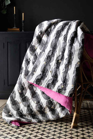 The Hot Pink & Gold Star Print Reversible Quilt in King-Size draped across a wicker chair.