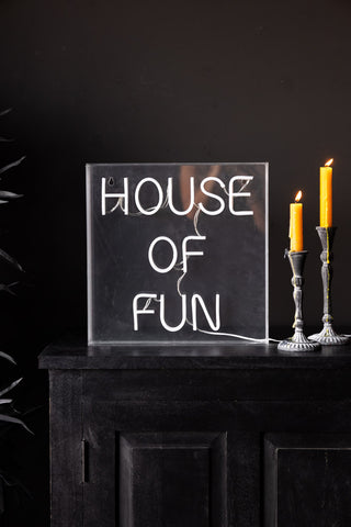 The House Of Fun Neon Light Box switched off and styled on a black unit next to two lit candles.