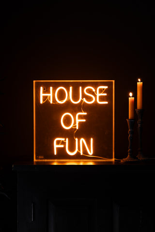 The House Of Fun Neon Light Box illuminated and styled on a surface next to two lit candles.