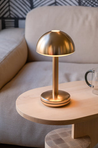 The Humble - Domed Cable-Free Mood Lighting Lighting in Gold displayed on a table in front of a sofa.