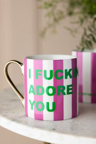 The I Fucking Adore You Stripe Mug styled on a marble surface with another mug and a plant in the background.