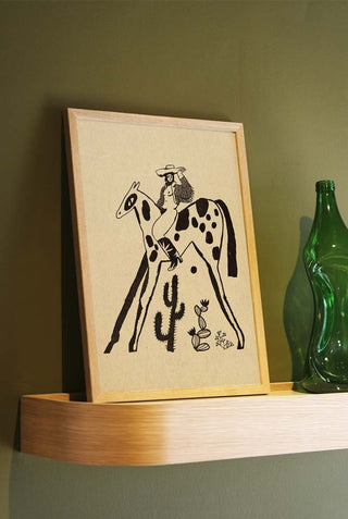 A cool cowgirl in a jacket and with cowboy boots sat on a horse. The art print is displayed on oak shelves, leaning against a green wall.