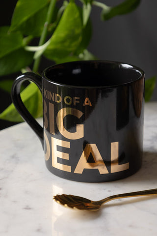 The I'm Kind Of A Big Deal Mug styled on a white marble table with a spoon, and a plant in the background.