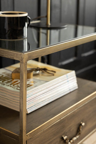 Detail shot of an industrial style bedside table seen from an angle, styled with magazines, a heart ornament, a mug and a lamp on.