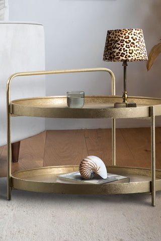 The Industrial Style Two-Tier Coffee Table Gold styled with a lamp, glass, book and shell ornament on.