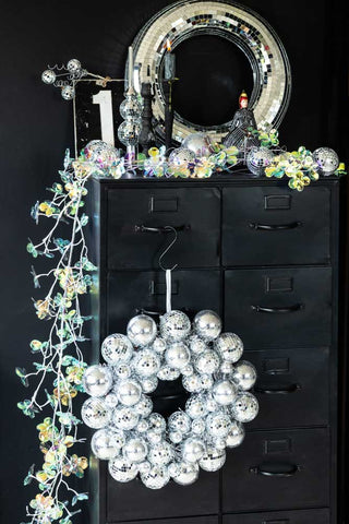 The Silver Disco Ball Christmas Wreath on a black cabinet styled with iridescent accessories.