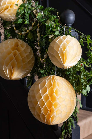 The Set Of 2 Ivory Honeycomb Ball Decorations hung on a black banister with green leaf decorations.