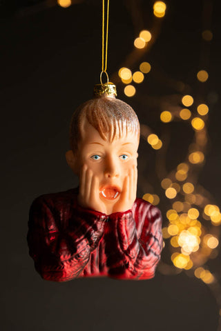 The Kevin Inspired Christmas Tree Decoration hanging in front of a dark wall with fairy lights.