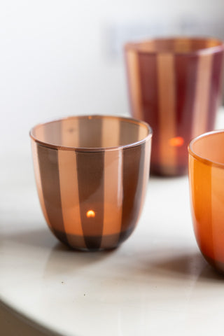 The Khaki Striped Tealight Holder - Short with a lit tealight inside, displayed on a table with two other tealight holders.