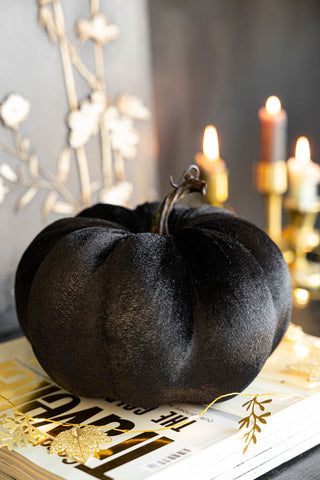 The Large Black Velvet Pumpkin displayed on a book with fairy lights, with lit candles in candlestick holders in the background.