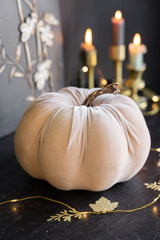 The Large Cream Velvet Pumpkin displayed on a dark wooden surface with fairy lights and lit candles in the background.