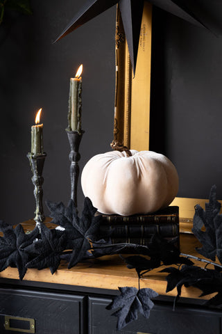 The Large Cream Velvet Pumpkin displayed on a wooden surface with books, maple garland and candle.