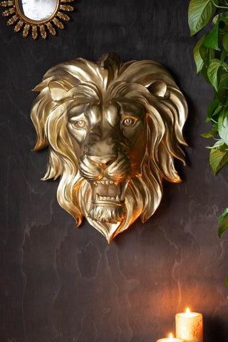 The Large Gold Lion Head Wall Art seen on a dark wall, styled with some lit candles a plant and a gold decorative mirror.