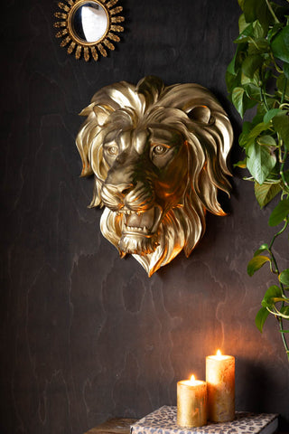 The Large Gold Lion Head Wall Art styled on a dark wall, with a mirror, plant and some lit candles.