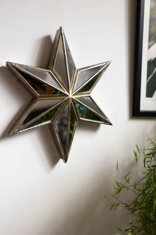 The Large Mirrored Star Wall Decoration styled on a white wall next to an art print and a plant.