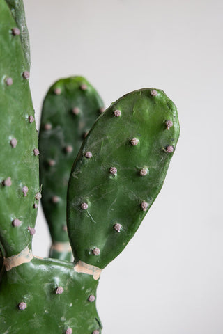 A close up of the top of a faux cactus plant against a white wall. 